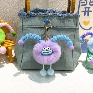 Close-up of purple plush monster keychain with blue horns on a denim bag