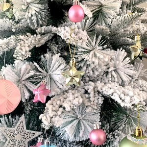 Detail of assorted pink and gold Christmas ornaments on a snow-flocked festive tree
