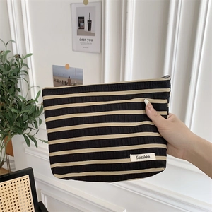 Detail of striped canvas toiletry bag with black and beige patterns and brand label