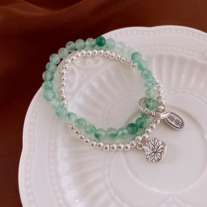 Detail of green jade beads and silver charms with lotus leaf on a white porcelain plate
