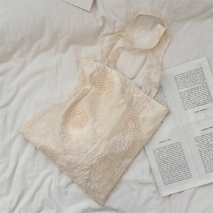 Detailed view of floral embroidery on cream canvas tote bag with French lace texture