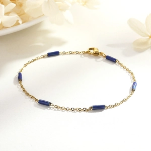 Détail d'un bracelet chaîne fine dorée avec perles tubes bleu foncé et fermoir mousqueton