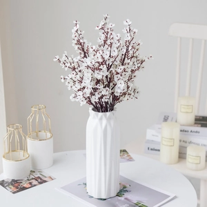 Detailed shot of white artificial flower bouquet in modern geometric ceramic vase arrangement.