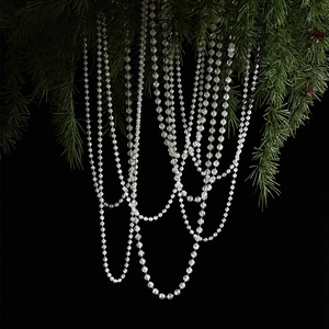 Transparent beaded Christmas tree garland hanging on green pine branches with black background