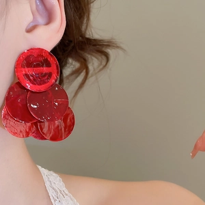 Detail of red tiered round sequin earrings worn by a model with a glossy finish