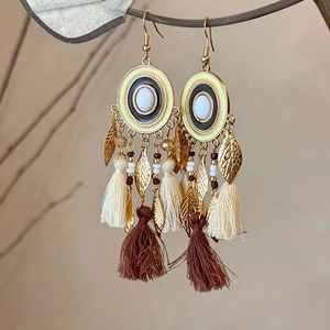 Detail of bohemian tassel earrings with gold leaf charms and white bead accents
