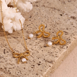 Detail shot of golden bow necklace and pearl earrings on a natural stone surface