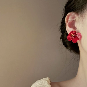 Elegant 3D red flower stud earrings with gold stamen worn by model on beige background