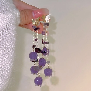 Close-up of long tassel earrings with purple lily flowers and golden butterfly accents