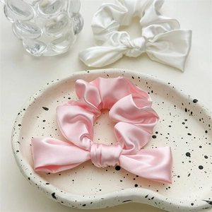 Close-up of satin scrunchies in pink and white with bow detail on a ceramic plate