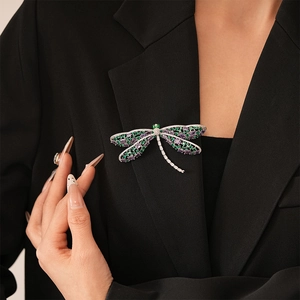 Detailed view of an elegant dragonfly brooch with purple and green crystals on black suit