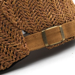Macro view of adjustable bronze buckle on brown woven sun hat with texture details