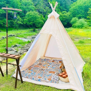 Detail view of a bohemian patterned picnic mat and teepee tent in a lush forest camping scene