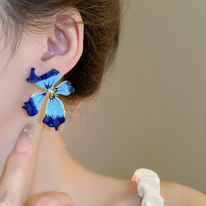 Gros plan d'un modèle portant des boucles d'oreilles pétales bleus dégradés et cœur doré