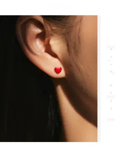 Close-up of red heart stud earrings with s925 silver edges worn on ear with soft lighting