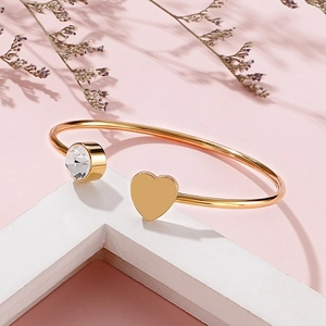 Dettaglio del bracciale rigido a cuore dorato con zircone su uno sfondo rosa morbido