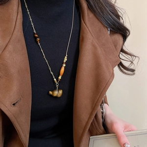 Detail of tiger eye gourd pendant on long necklace paired with winter coat styling