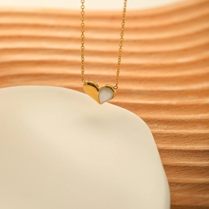 French heart necklace with gold chain and shell inlay on a white ceramic dish