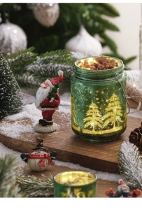 Close-up of green glass Christmas candle holder with golden tree etching and pine cone detail