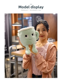 Close-up of cute light green plush latte cup toy held by hands in a cozy cafe setting