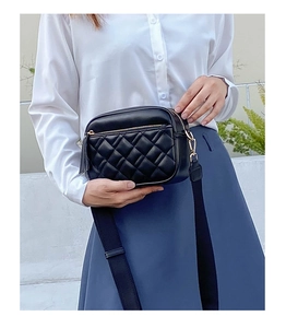 Detail of black quilted camera bag with gold zipper and wide fabric shoulder strap
