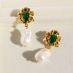 Vintage gold vine earrings with emerald gems and large baroque pearls on beige texture