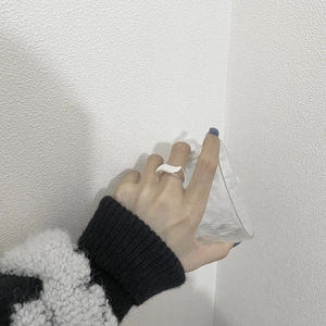 Close-up of a minimalist S925 sterling silver wavy ring worn on a hand holding glass