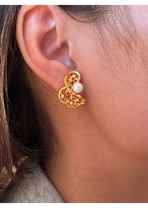 Close-up of golden hollow twisted earrings with white pearl and sparkling crystals