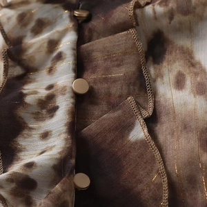 Macro view of brown tie-dye fabric with gold metallic threads and ruffles