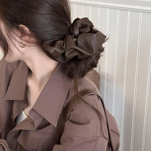 Detailed view of an oversized brown leather-like scrunchie on a stylish low hair bun