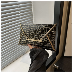 Detail of black crocodile pattern envelope clutch with elegant gold metal trim
