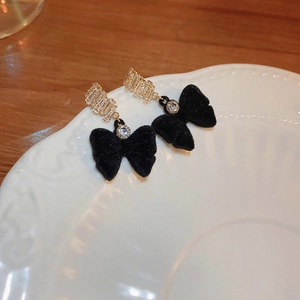 Detailed view of elegant bow earrings with black flocking and zircon on a ceramic plate