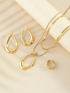 Detailed close-up of golden wavy necklace, earrings and ring set in abstract organic design