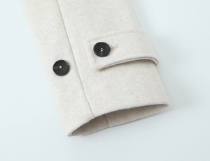Detailed close-up of beige wool coat cuffs with black resin buttons and fine stitching