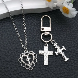 Detailed view of silver cross and heart pendants on necklace and keychain on black leather