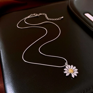 Detailed close-up of a zircon daisy pendant on a silver snake chain over black leather