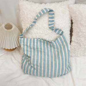 Close-up of blue and white striped canvas shoulder bag on soft white bedding