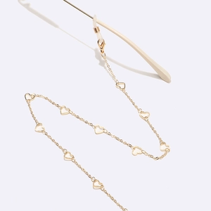 Detail of golden metal glasses chain featuring white heart charms and silicone loops