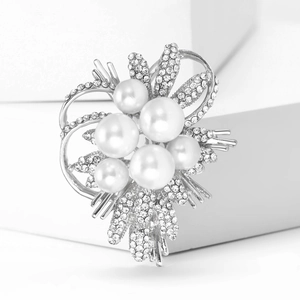 Detailed view of silver flower brooch with white pearls and rhinestones on a white block