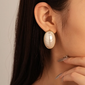 Macro shot of oval pearl stud earrings with gold plating on a model's ear