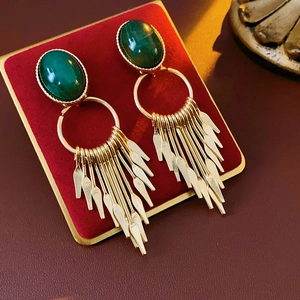 Detail of vintage gold earrings with green gemstones and tassels on velvet