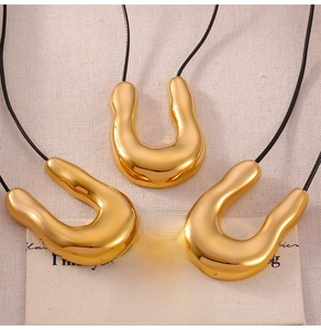Detailed shot of gold U-shaped pendants on black braided cords over a beige linen background