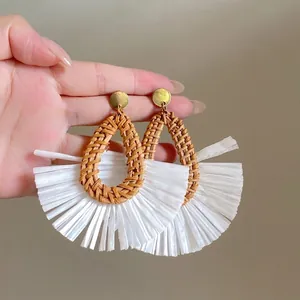 Close-up of fan-shaped raffia earrings with woven brown droplets and white fringe detail