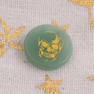 Detailed view of green aventurine round stone featuring a golden skull engraving