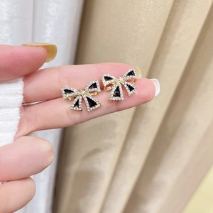 Detailed close-up of golden bow earrings with black inlay and sparkling zircon border