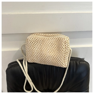 Detailed view of beige woven crossbody bag with zipper and thin cord strap on black chair
