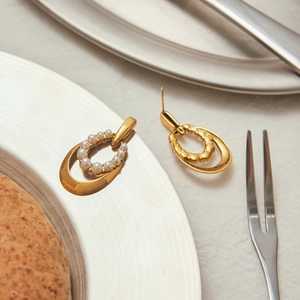 Detailed view of 18K gold plated oval earrings with pearl inlay on a metal plate