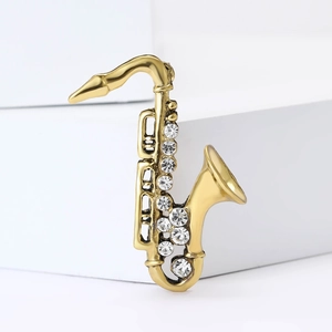 Golden saxophone brooch with enamel and crystals displayed on a clean white pedestal