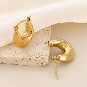Macro detail of glossy gold U-shaped chunky hoop earrings on elegant silk and stone