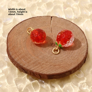 Macro shot of 13x19mm red strawberry glass charms with gold loops on wood background